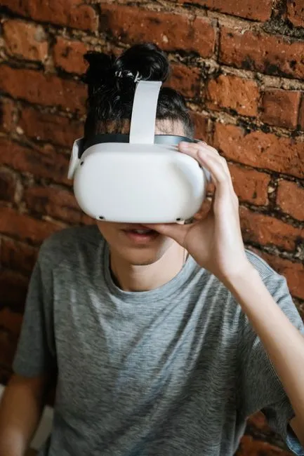 Jeune adulte portant un casque VR, vivant la réalité virtuelle contre un mur en briques à l'intérieur.