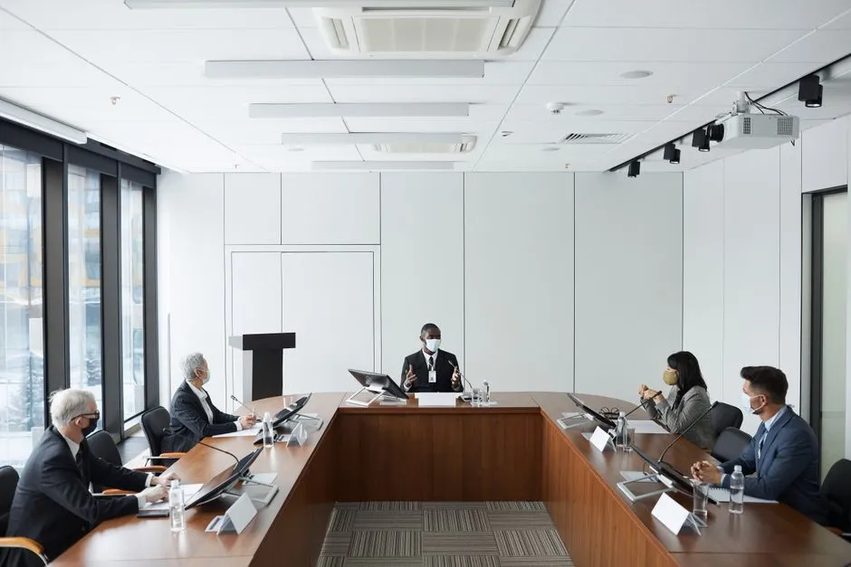 Des professionnels d'affaires dans une salle de conférence portant des masques, mettant en avant la diversité et la coopération.
