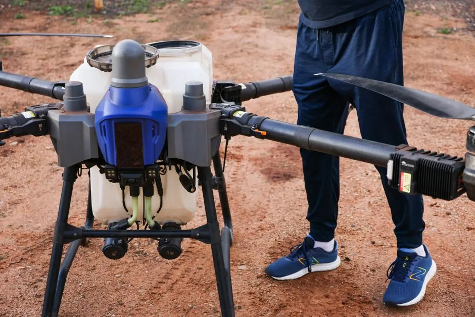 Gros plan sur un drone agricole utilisé dans un champ de terre, piloté par une personne.