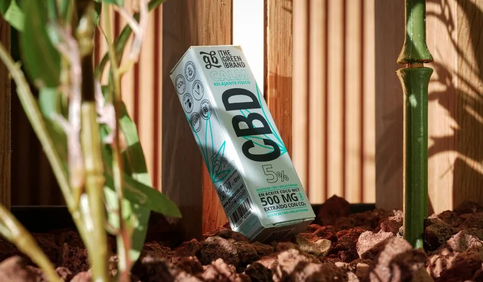 Emballage d'huile de CBD parmi les plantes et la lumière du soleil, soulignant la détente et les éléments naturels.