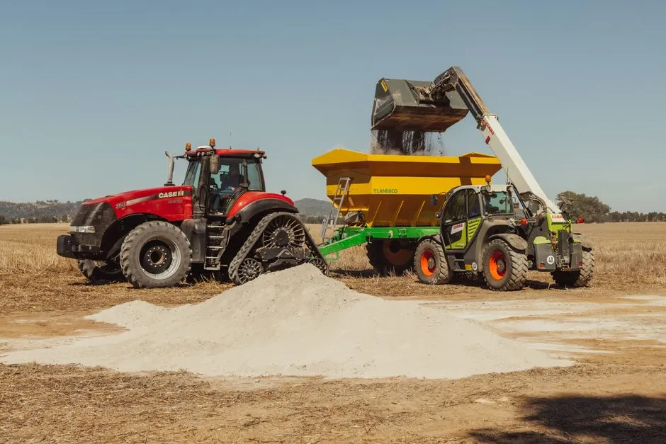 Un tracteur et une chargeuse travaillent ensemble pour épandre des engrais sur un champ.