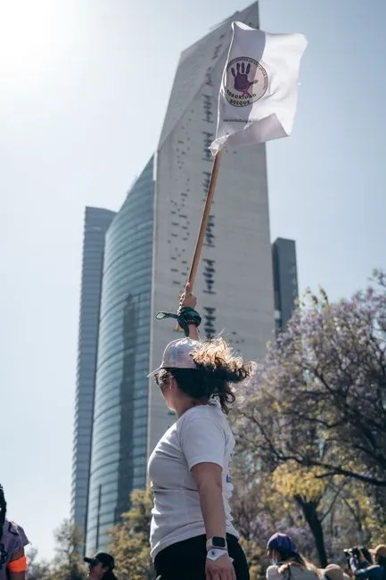 Femme tenant un drapeau de protestation près d'un gratte-ciel à Mexico, illustrant l'activisme urbain.