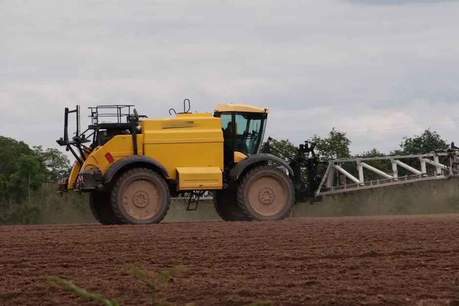 Tracteur jaune dans un champ, utilisé pour des travaux agricoles sous un ciel nuageux.